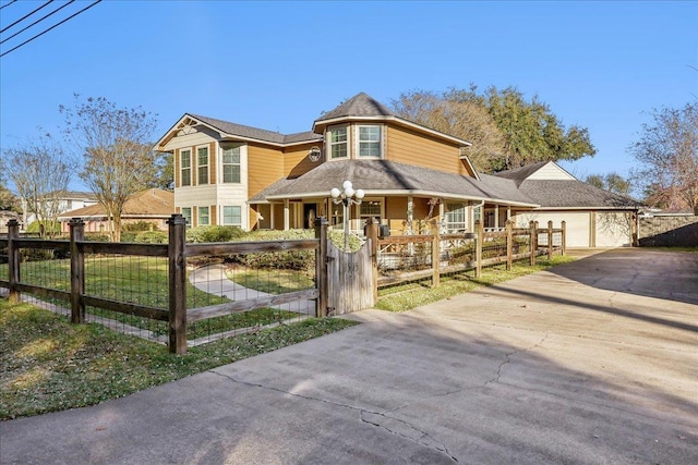 victorian-style house featuring covered porch, driveway, a fenced front yard, and a garage