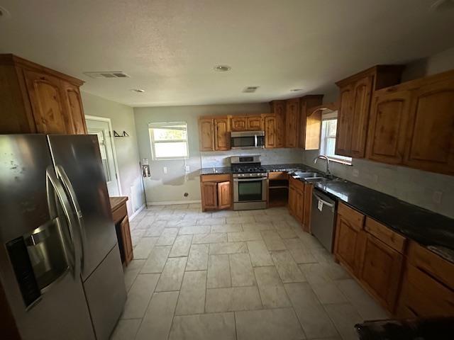 320 Meadow Dr, Bridge City, TX 77611 - kitchen featuring appliances with stainless steel finishes, a sink, brown cabinetry, and dark countertops