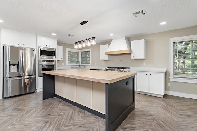 kitchen with appliances with stainless steel finishes, butcher block counters, custom range hood, a sink, and white cabinets