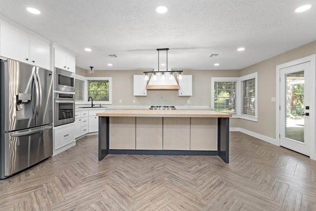 kitchen with stainless steel appliances, wooden counters, a sink, baseboards, and white cabinetry