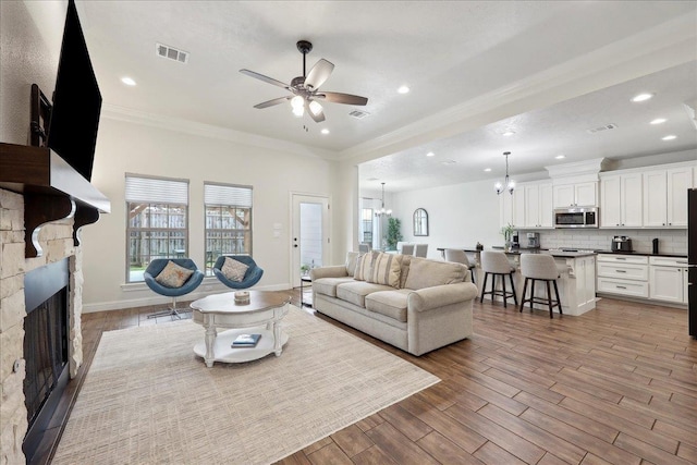 9270 Pampas St, Beaumont, TX 77713 - living room featuring wood finished floors, ornamental molding, ceiling fan with notable chandelier, a stone fireplace, and visible vents
