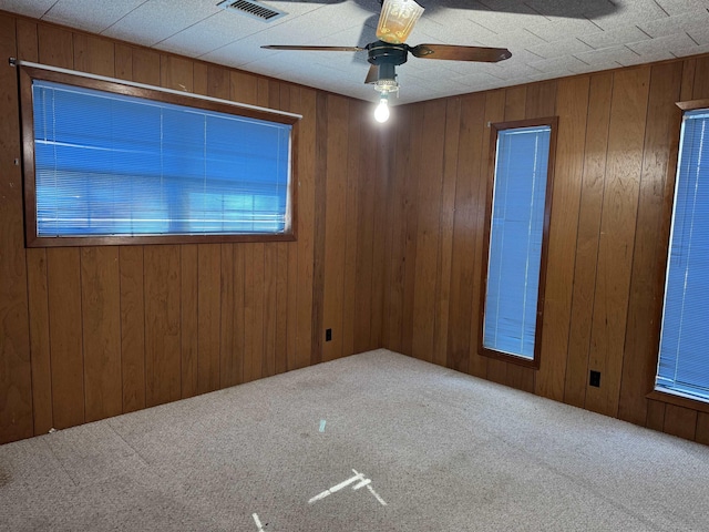 carpeted empty room featuring wooden walls, a ceiling fan, and visible vents