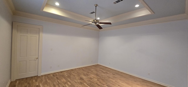 empty room featuring visible vents, a raised ceiling, wood finished floors, and crown molding