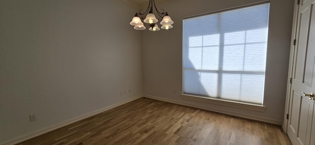 spare room with a notable chandelier, baseboards, and wood finished floors