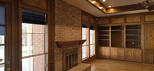 unfurnished living room with built in shelves, ornamental molding, a tray ceiling, light wood-style floors, and a fireplace