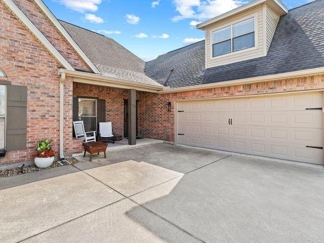 exterior space with concrete driveway, roof with shingles, brick siding, and covered porch