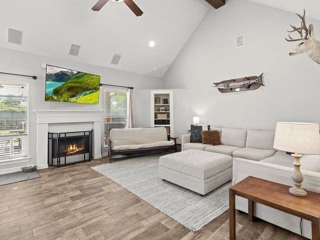 living room with a warm lit fireplace, visible vents, ceiling fan, and wood finished floors