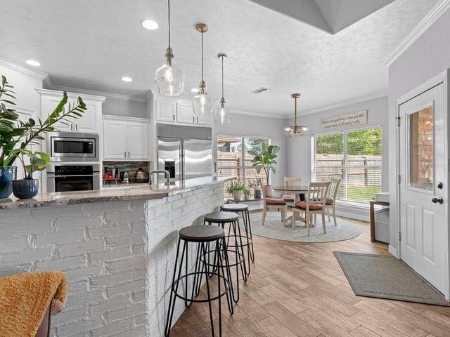kitchen featuring ornamental molding, white cabinets, light wood finished floors, and built in appliances