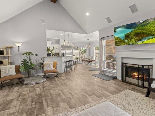 interior space with high vaulted ceiling, beamed ceiling, light wood-style flooring, a glass covered fireplace, and visible vents