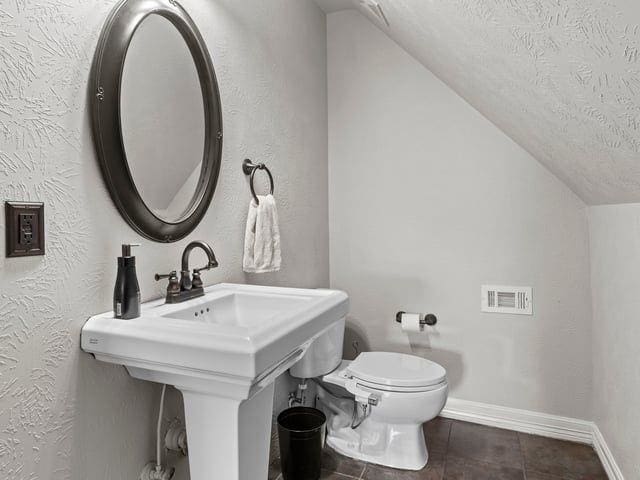 half bath with baseboards, toilet, a textured wall, a textured ceiling, and lofted ceiling
