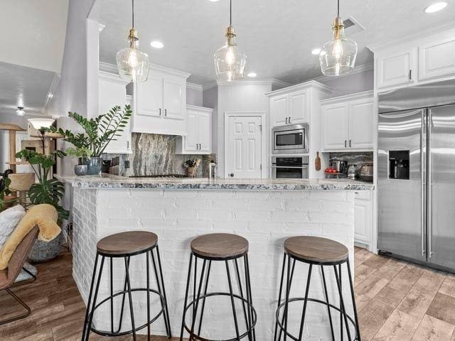 kitchen with light wood-type flooring, built in appliances, a breakfast bar area, and ornamental molding