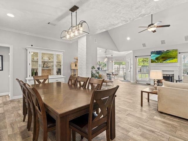 dining space featuring baseboards, a fireplace, crown molding, light wood-style floors, and ceiling fan with notable chandelier