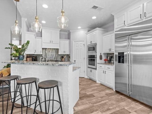 kitchen featuring built in appliances, visible vents, ornamental molding, and decorative backsplash
