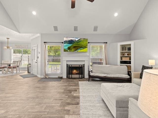 living area featuring visible vents, wood finished floors, a warm lit fireplace, and ceiling fan