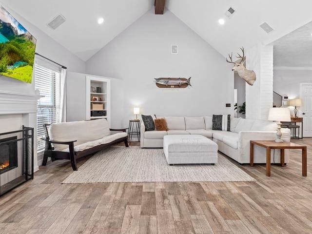 living area with high vaulted ceiling, a glass covered fireplace, visible vents, wood finished floors, and beam ceiling