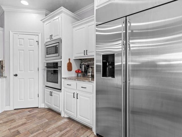kitchen with ornamental molding, light stone countertops, light wood-type flooring, and stainless steel appliances