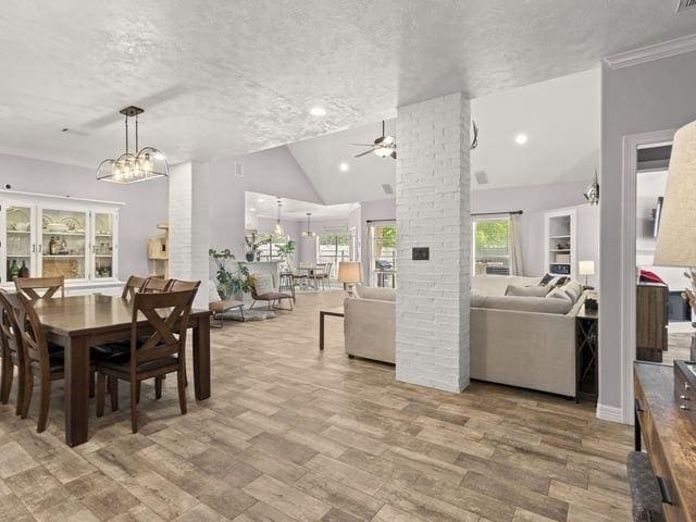 dining area featuring high vaulted ceiling, ceiling fan with notable chandelier, a textured ceiling, and wood finished floors