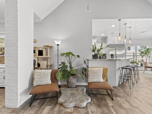 living area featuring wood finished floors, visible vents, ornamental molding, and vaulted ceiling