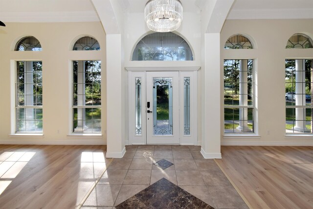 foyer featuring a notable chandelier, light hardwood / wood-style floors, ornamental molding, and a wealth of natural light