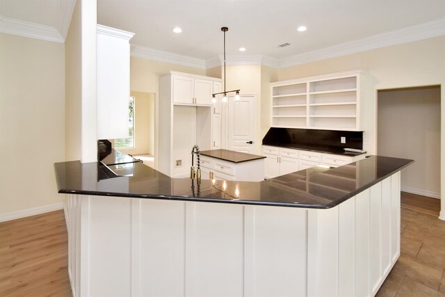 kitchen featuring kitchen peninsula, white cabinetry, hanging light fixtures, and ornamental molding