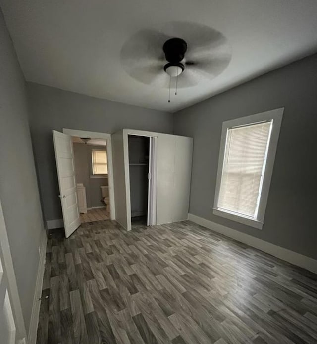 unfurnished bedroom featuring multiple windows, dark hardwood / wood-style floors, ensuite bath, and ceiling fan