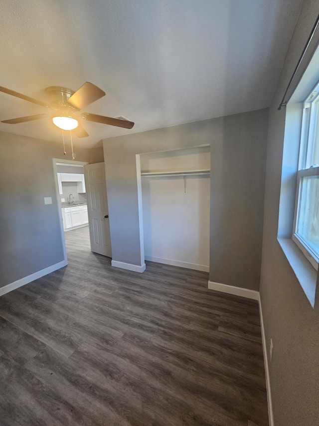 unfurnished bedroom with ceiling fan, a closet, dark wood-type flooring, and sink