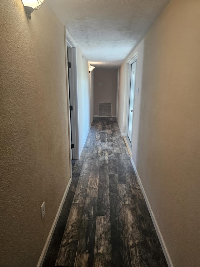 hallway with a textured ceiling and dark wood-type flooring