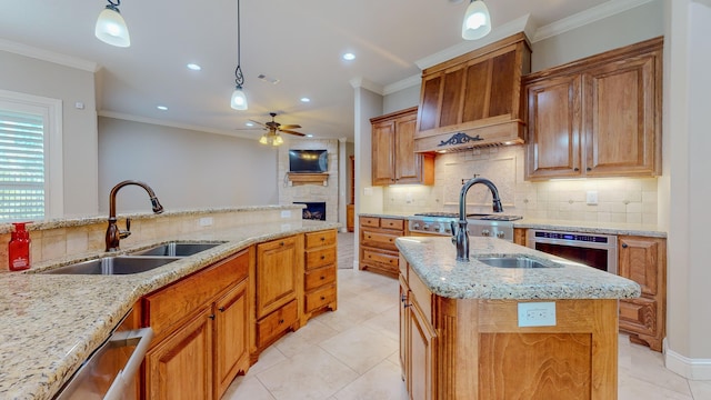 kitchen with light stone countertops, backsplash, a kitchen island with sink, sink, and decorative light fixtures