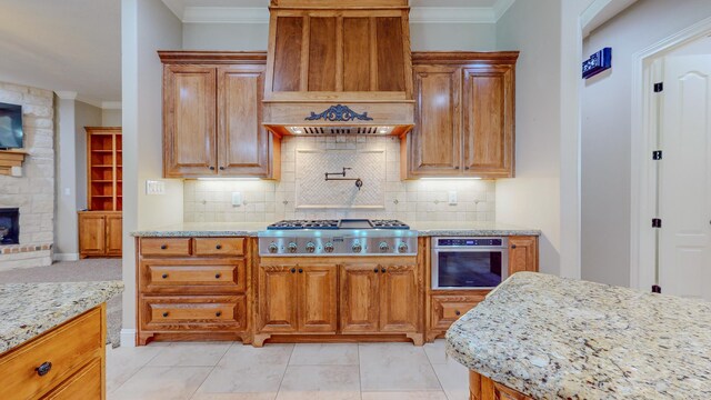 kitchen with decorative backsplash, appliances with stainless steel finishes, a stone fireplace, and custom exhaust hood