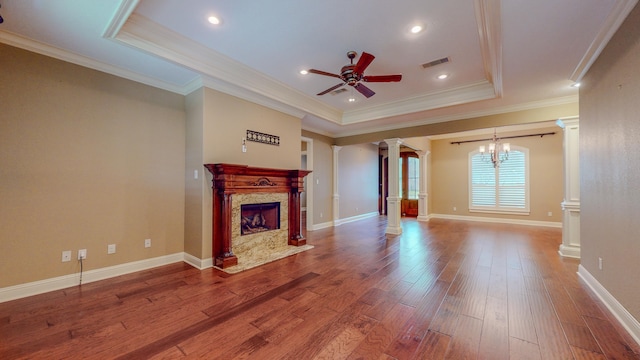 unfurnished living room with ornate columns, a raised ceiling, a fireplace, ceiling fan with notable chandelier, and ornamental molding