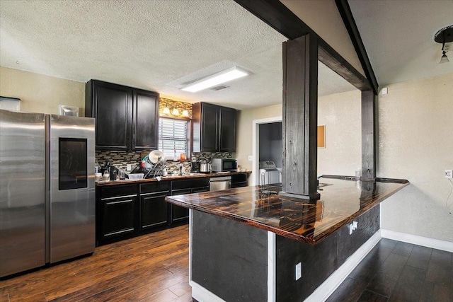 kitchen featuring decorative backsplash, appliances with stainless steel finishes, a kitchen bar, kitchen peninsula, and dark wood-type flooring