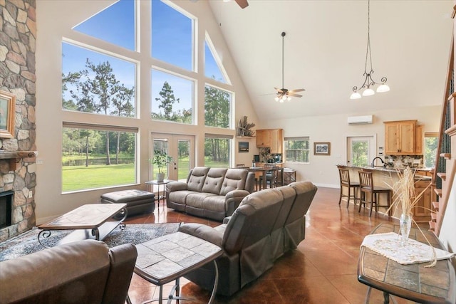 living room featuring french doors, a stone fireplace, tile patterned floors, a towering ceiling, and ceiling fan with notable chandelier