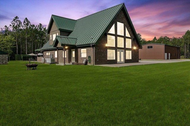 back house at dusk with an outdoor structure, a yard, and central AC