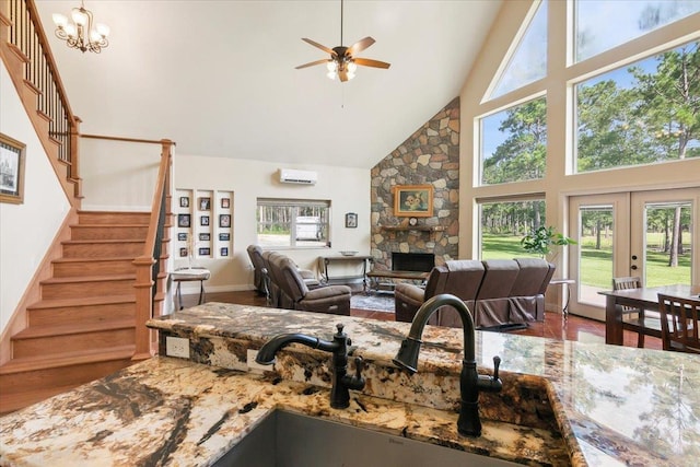 living room featuring ceiling fan with notable chandelier, a stone fireplace, high vaulted ceiling, and french doors