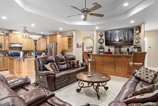 living room with ceiling fan, a raised ceiling, and light tile patterned floors