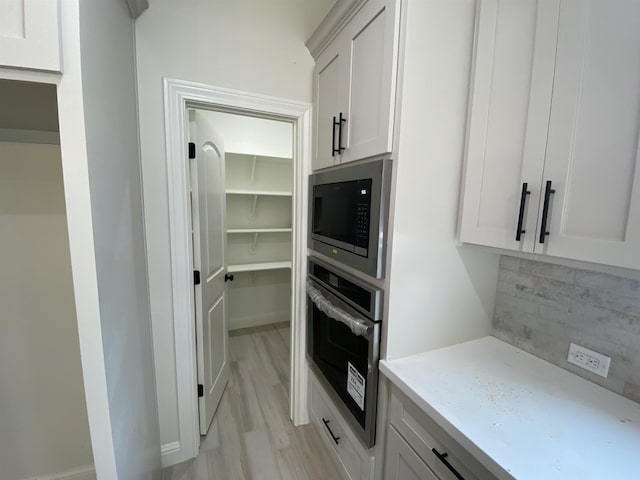 kitchen with white cabinets, decorative backsplash, light wood-type flooring, and appliances with stainless steel finishes