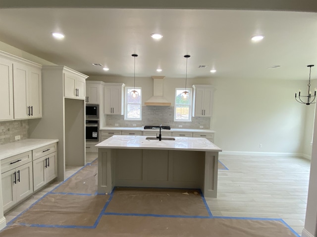 kitchen featuring decorative light fixtures, premium range hood, a center island with sink, and sink