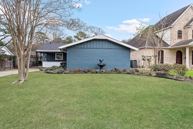 view of front of house with brick siding, a shingled roof, a front yard, fence, and cooling unit