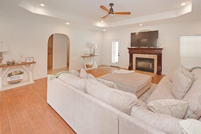 living room featuring a tiled fireplace, a raised ceiling, and light hardwood / wood-style floors