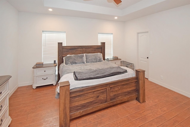 bedroom featuring ceiling fan, a tray ceiling, and light hardwood / wood-style floors