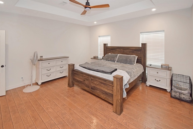 bedroom with ceiling fan, a raised ceiling, and light hardwood / wood-style floors