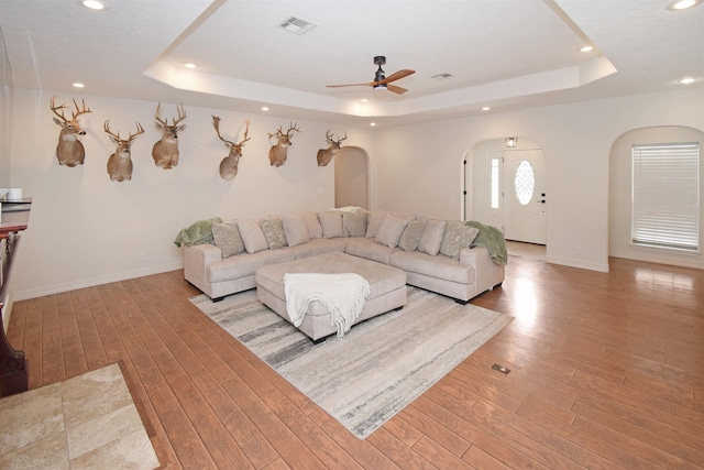 living room with ceiling fan, light hardwood / wood-style floors, and a tray ceiling