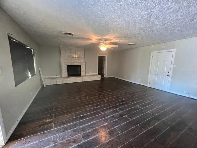 unfurnished living room with ceiling fan, a tile fireplace, and a textured ceiling