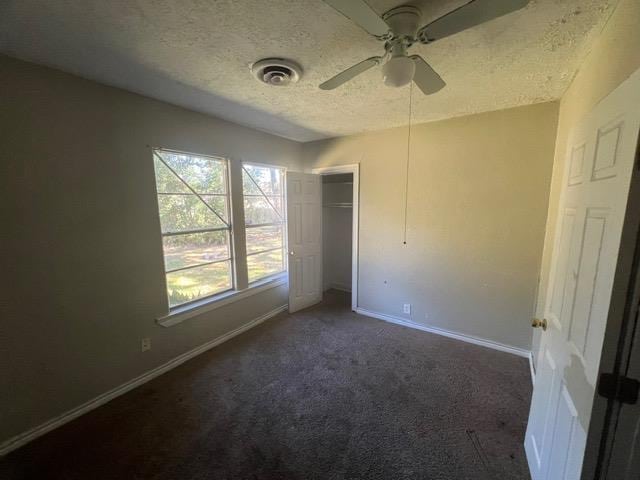 unfurnished bedroom featuring a textured ceiling, ceiling fan, a closet, and dark colored carpet