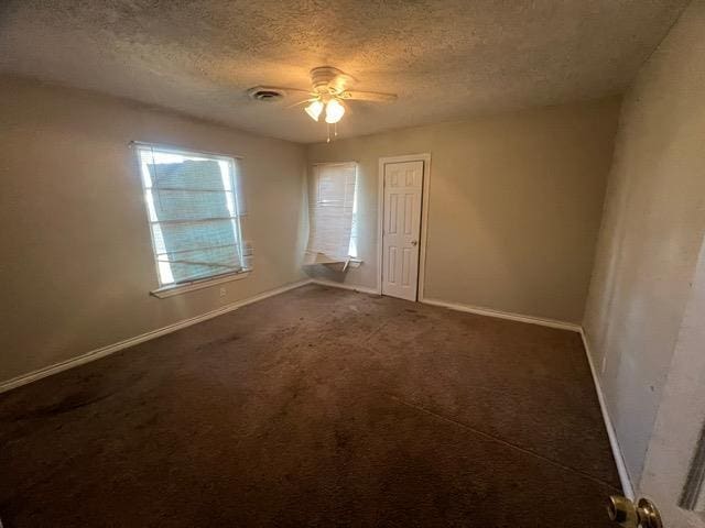 spare room featuring ceiling fan, dark carpet, and a textured ceiling