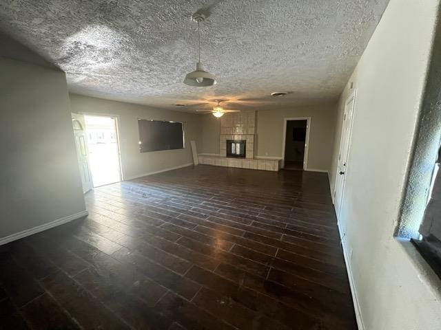 unfurnished living room with ceiling fan, dark hardwood / wood-style flooring, and a tiled fireplace