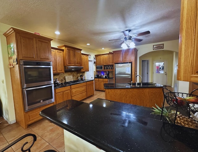 8135 Dawn Dr, Beaumont, TX 77705 - kitchen with stainless steel appliances, backsplash, a textured ceiling, light tile patterned flooring, and brown cabinets