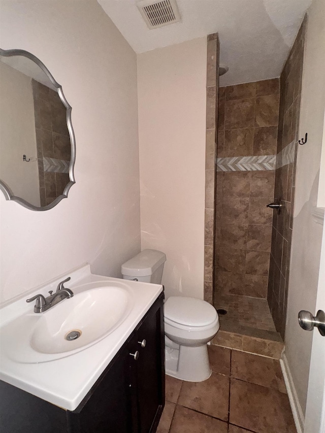 bathroom with tile patterned flooring, vanity, toilet, and a tile shower