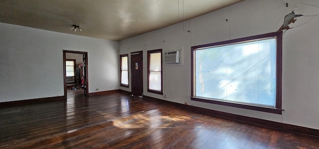 empty room with dark wood-type flooring, a healthy amount of sunlight, and a wall unit AC