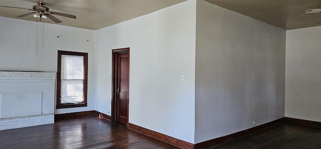 unfurnished room featuring dark wood-type flooring, ceiling fan, and a brick fireplace